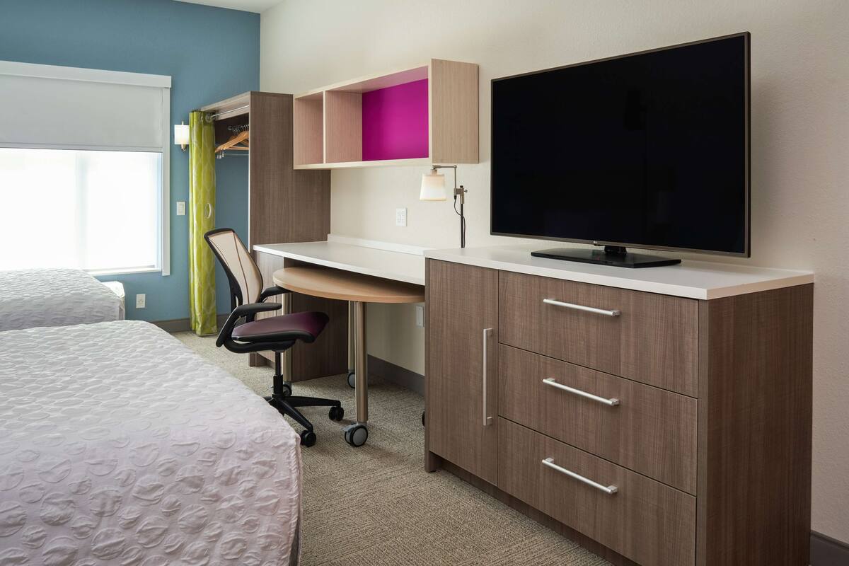 Ein Hotelzimmer mit einem Bett, einem Schreibtisch mit Stuhl, einem Fernseher und einem Kleiderschrank.