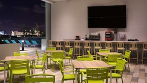 A rooftop bar with green chairs and tables, a flat-screen TV, and a coffee machine. - Home2 Suites by Hilton Ft. Lauderdale Downtown, FL (Fort Lauderdale)