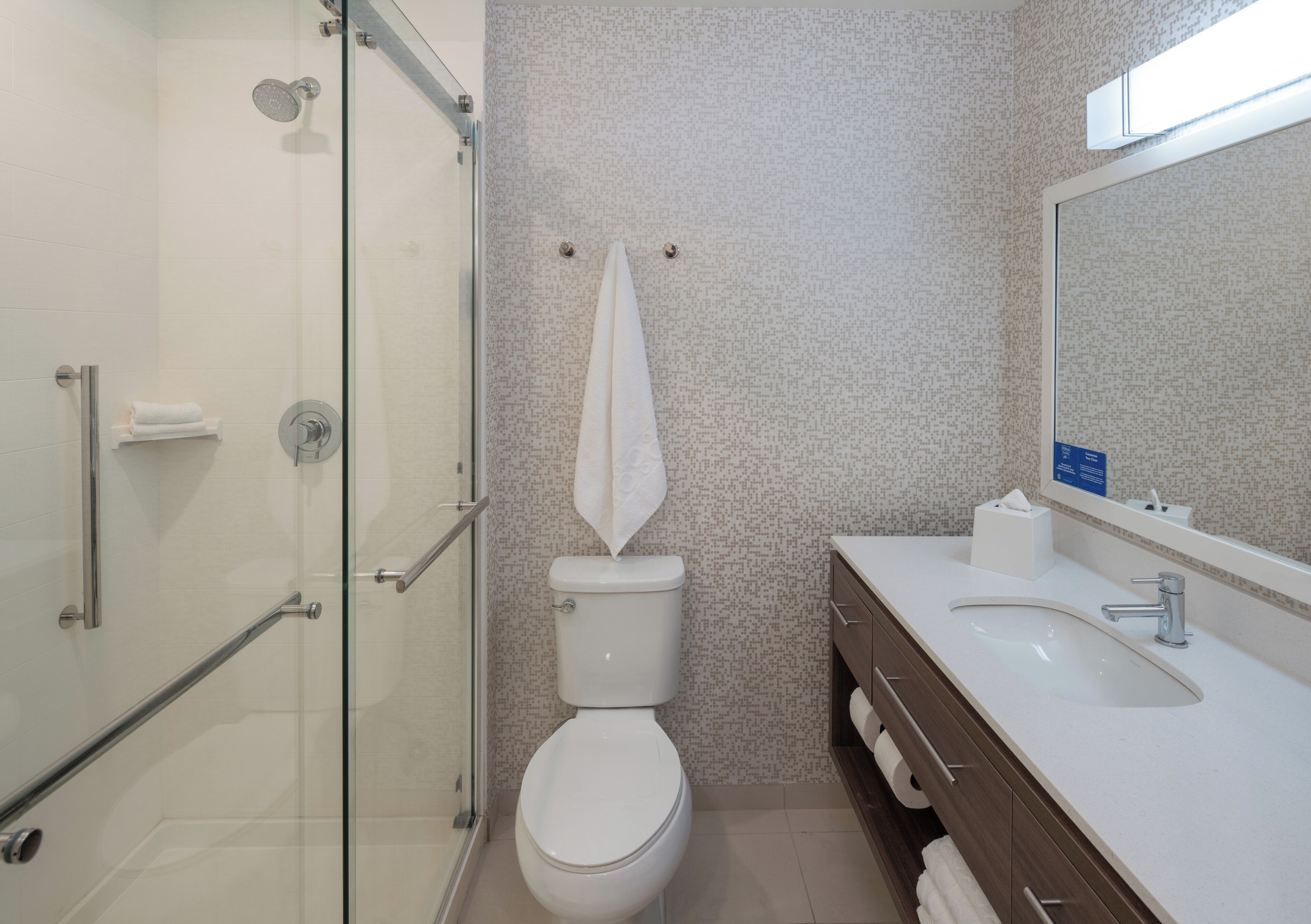 Une salle de bain moderne avec une douche à parois de verre, des toilettes blanches, un lavabo avec un miroir et une serviette accrochée au mur.