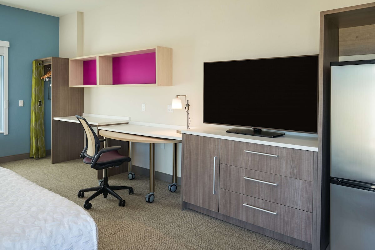 Ein modernes Hotelzimmer mit Bett, Schreibtisch, Stuhl und integriertem Fernseher.