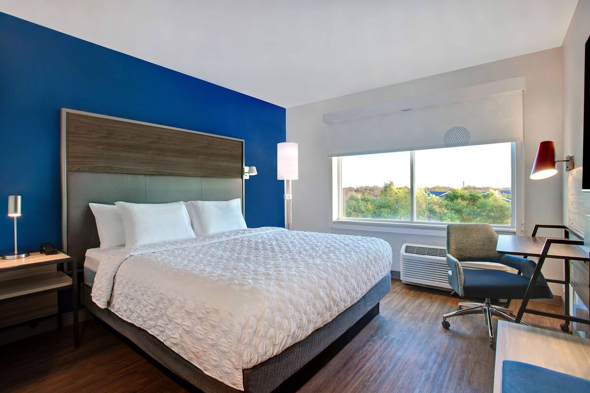 Habitación de hotel moderna con una cama grande, un escritorio con silla, una ventana con vistas y una lámpara roja.