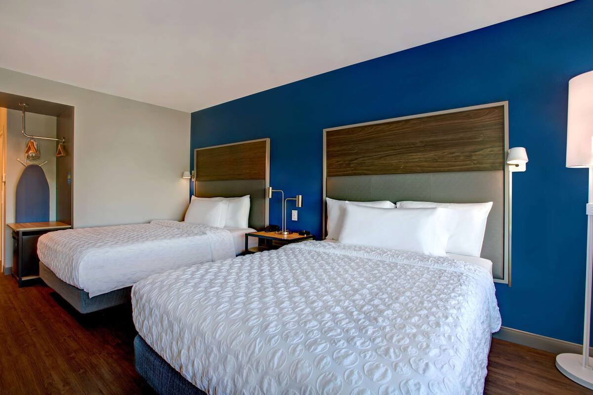 Habitación de hotel con dos camas, cabeceros de madera y una pared decorada en azul.