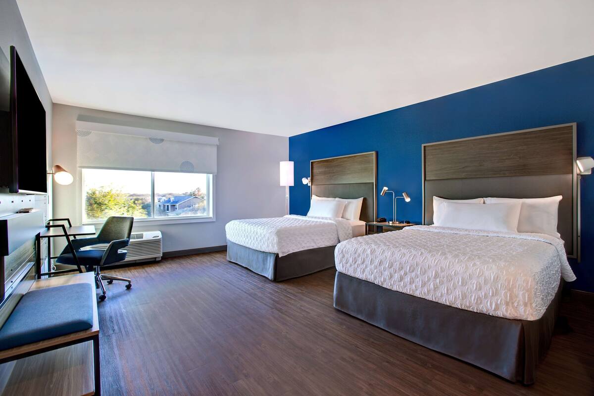 Habitación de hotel con dos camas, un escritorio, una silla, un televisor y un ventanal grande.