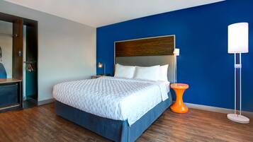A modern hotel room with a large bed, wooden flooring, and a blue accent wall.