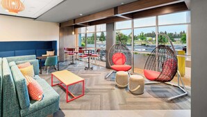 A modern lounge area with a blue sofa, red chairs, a hanging egg chair, and large windows offering a view of the outdoors. - Tru By Hilton Spokane Valley, WA (Spokane Valley)