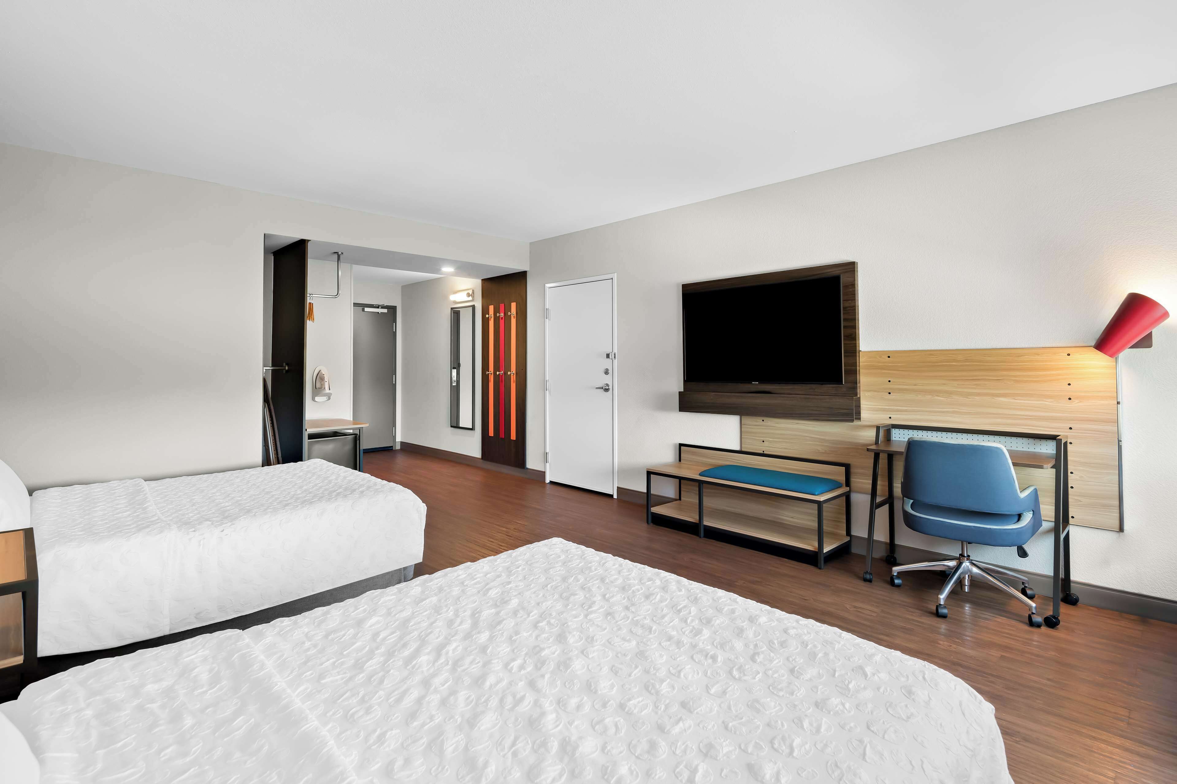 A hotel room with two beds, a desk with a chair, a TV, and a red lamp.