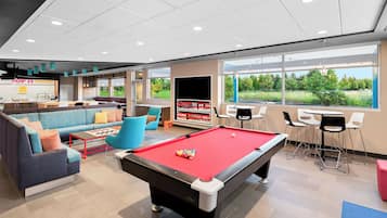 Un tavolo da biliardo in una moderna area lounge con divano e poltrone, una televisione e vista sul verde circostante.