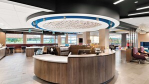 A modern reception area with a curved desk, seating, and a large window offering a view of greenery. - Tru By Hilton Spokane Valley, WA (Spokane Valley)