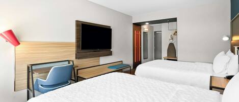 A hotel room with two beds, a TV mounted on the wall, a desk with a chair, and a mirror.
