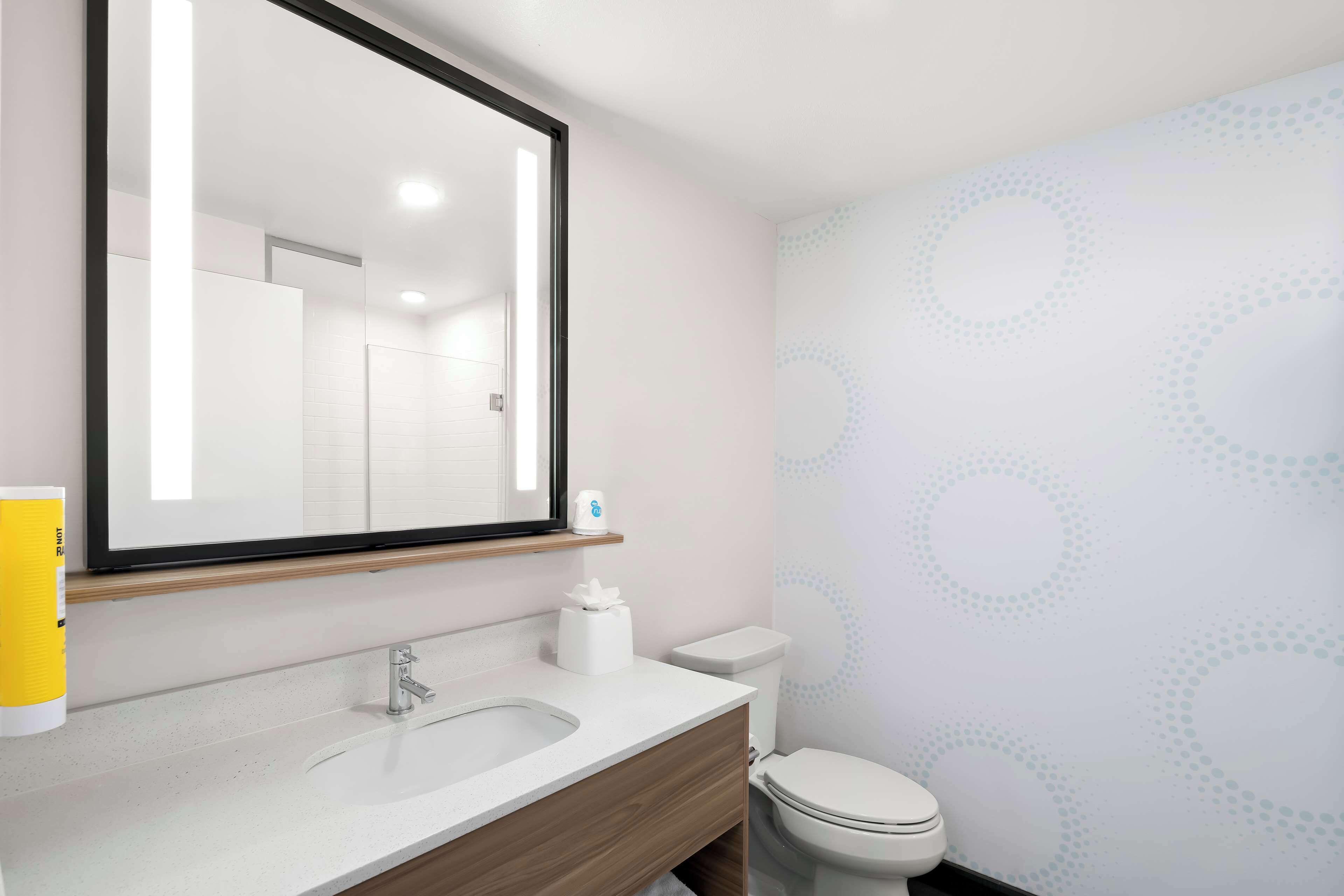 Un baño moderno con un espejo grande, un lavabo y un inodoro.