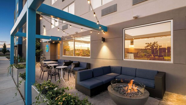 An outdoor seating area with a fire pit, blue furniture, and large windows overlooking a cityscape. - Tru By Hilton Spokane Valley, WA (Spokane Valley)
