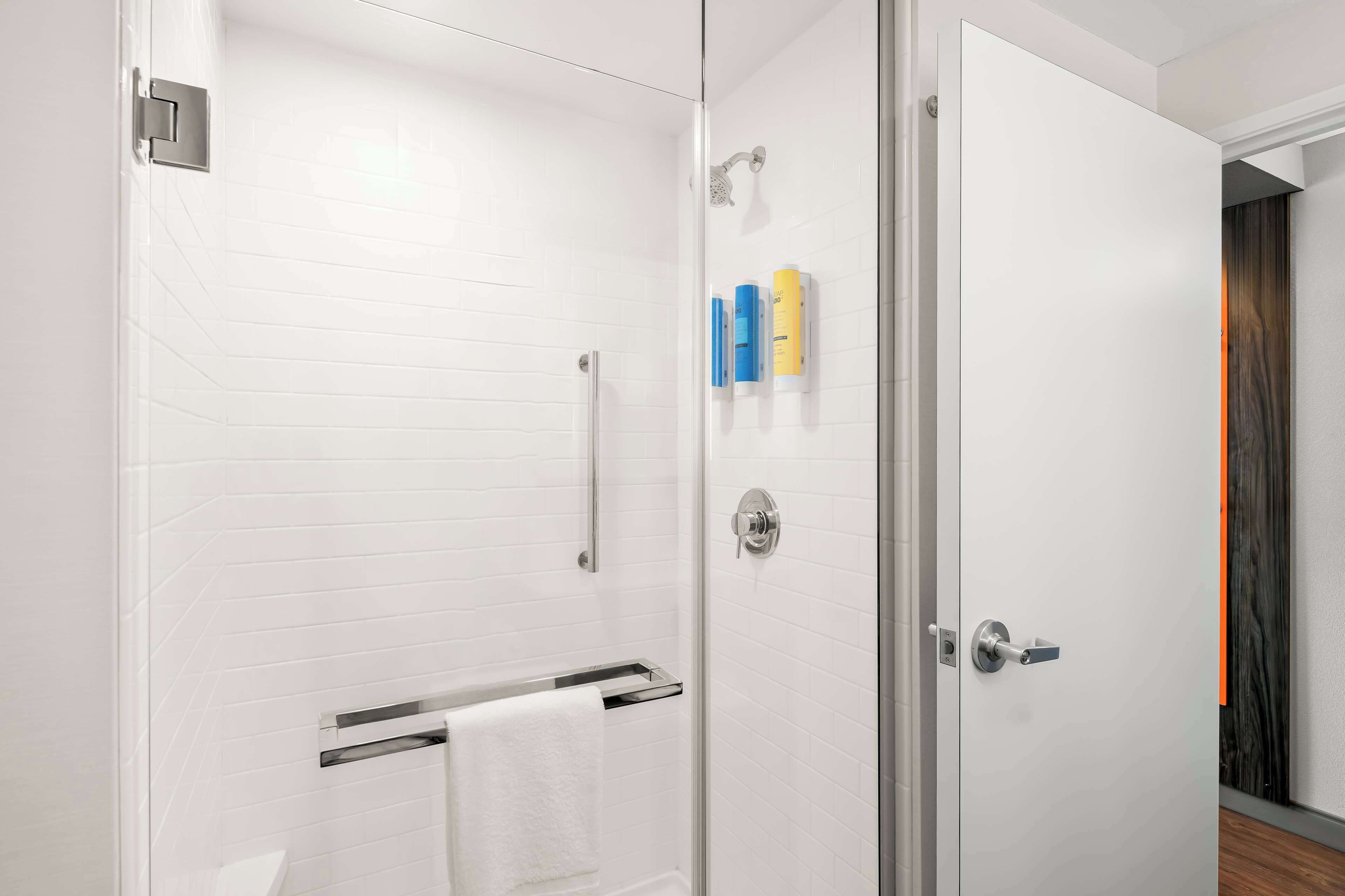 Un baño moderno con paredes de azulejos blancos, cabina de ducha de vidrio, toallero y artículos de aseo en la pared.