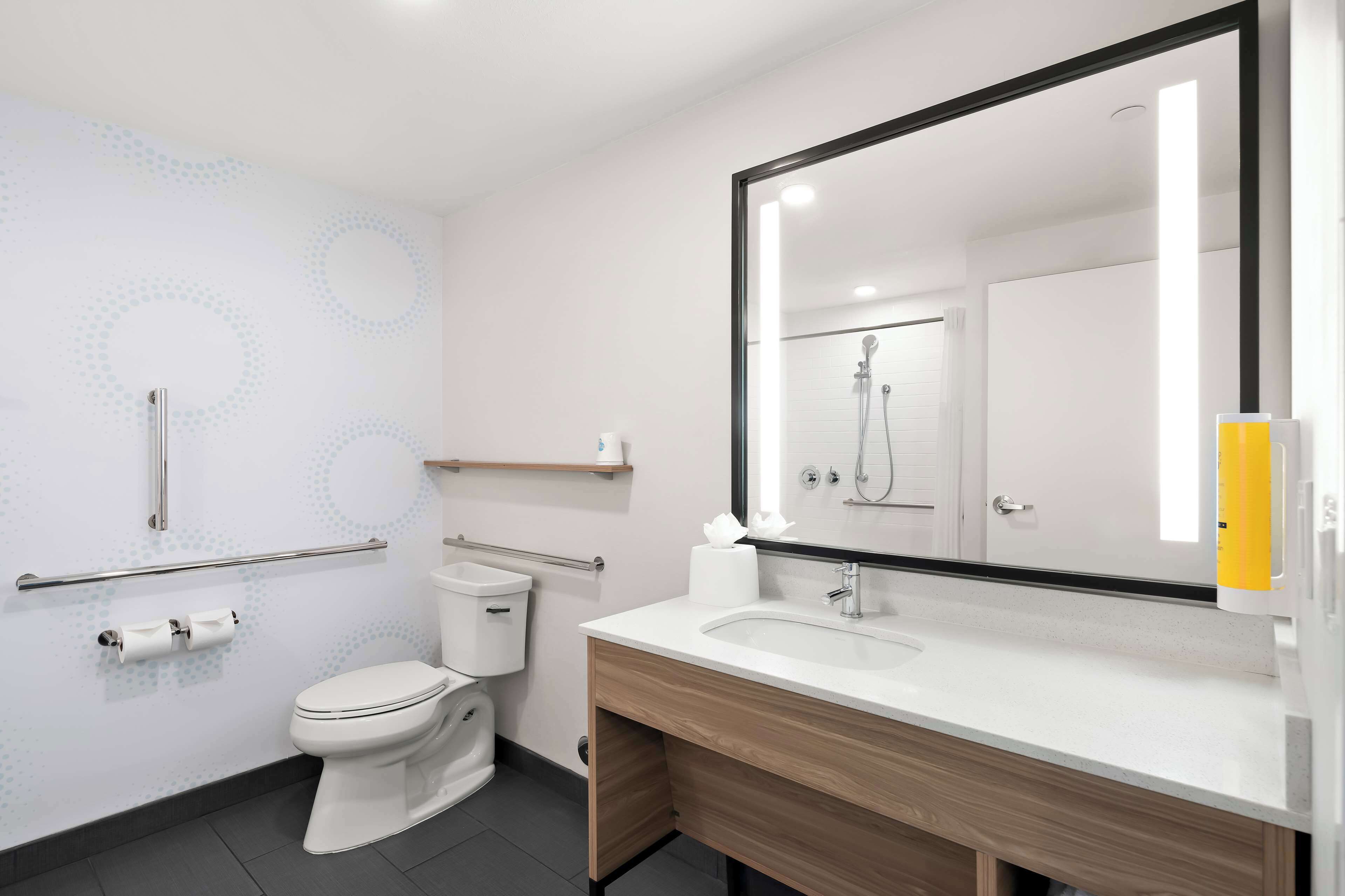 A modern bathroom with a toilet, bidet, vanity with sink, mirror, and towel dispenser.