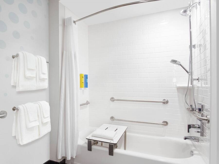 A modern bathroom with a white bathtub, grab bars, and a towel rack.