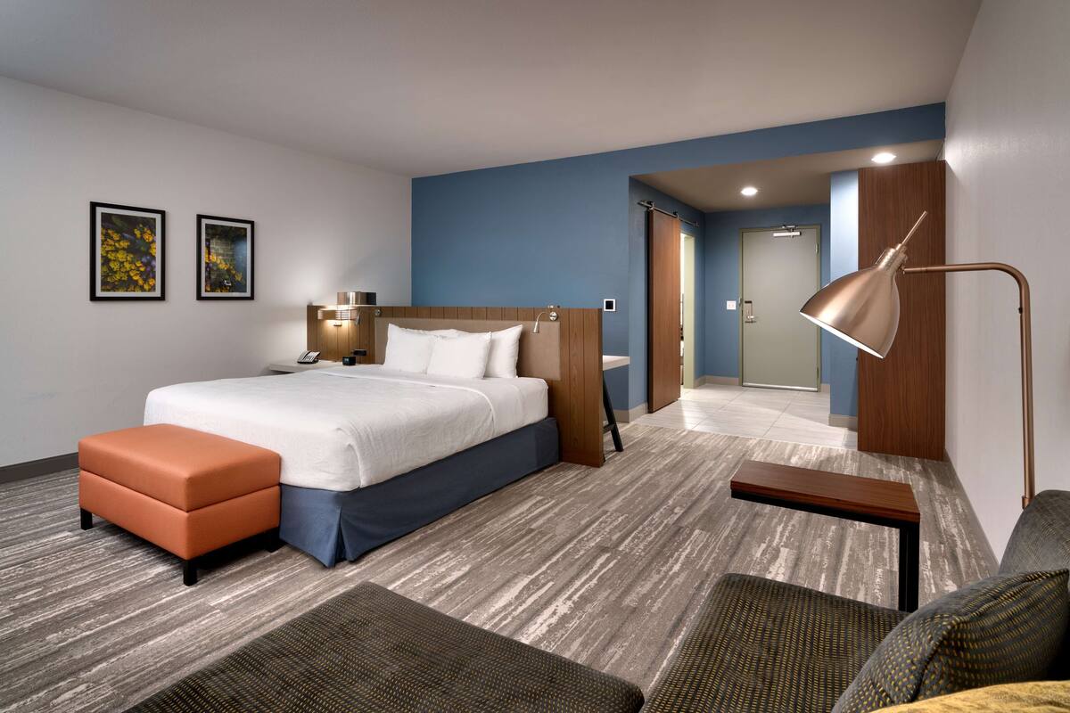 A modern hotel room with a bed, a desk, a chair, and a sofa.