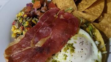 Une assiette avec un œuf au plat, une tranche de jambon de Parme, une salade de maïs et des chips de tortillas.
