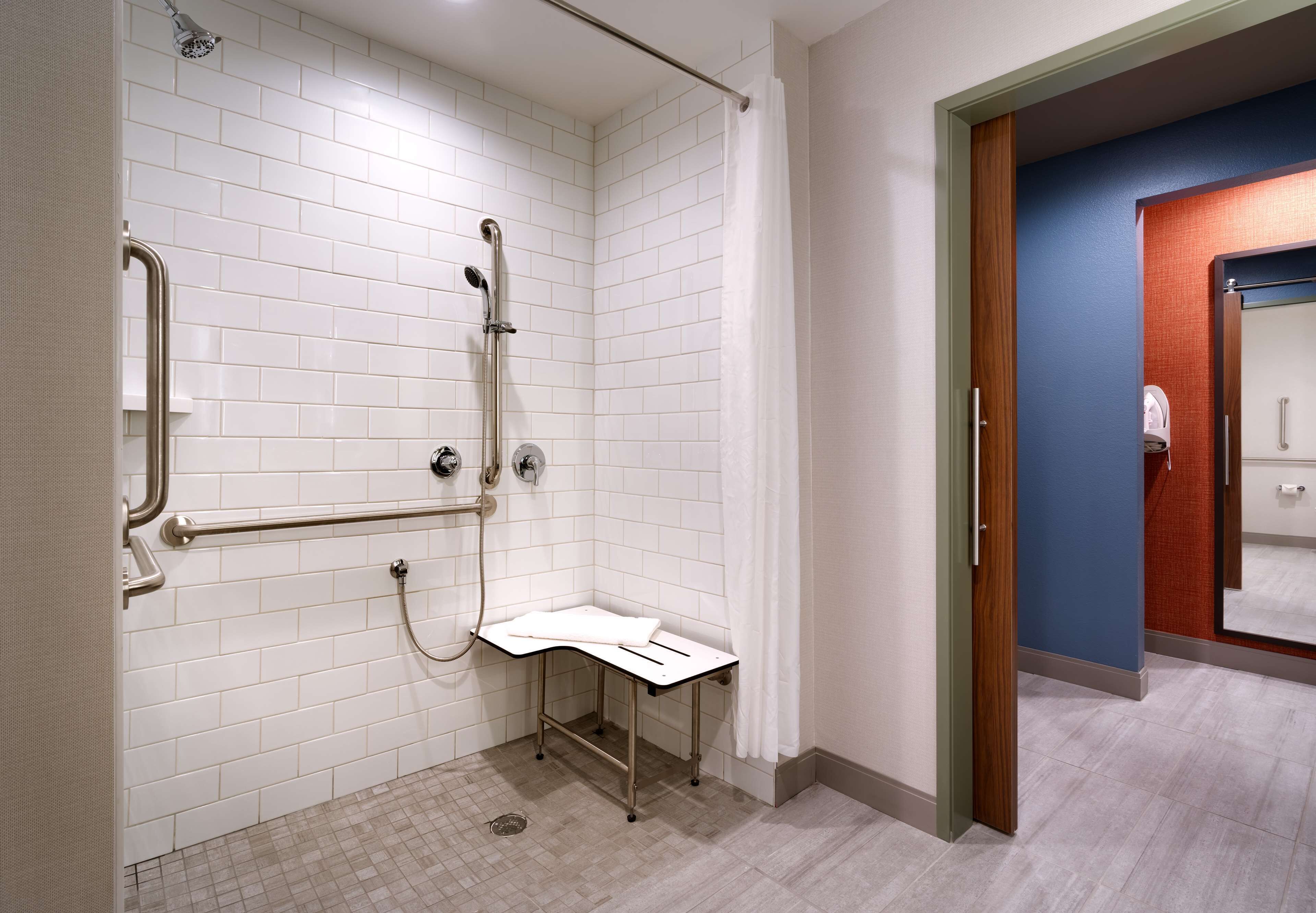 A bathroom with white tiled walls, a shower with a grab bar, and a small white bench.