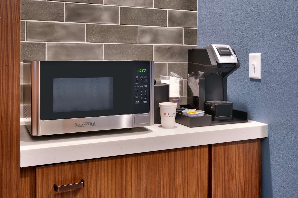 A microwave with a digital display, a coffee maker, and a container with Hilton Garden Inn branding on a countertop.