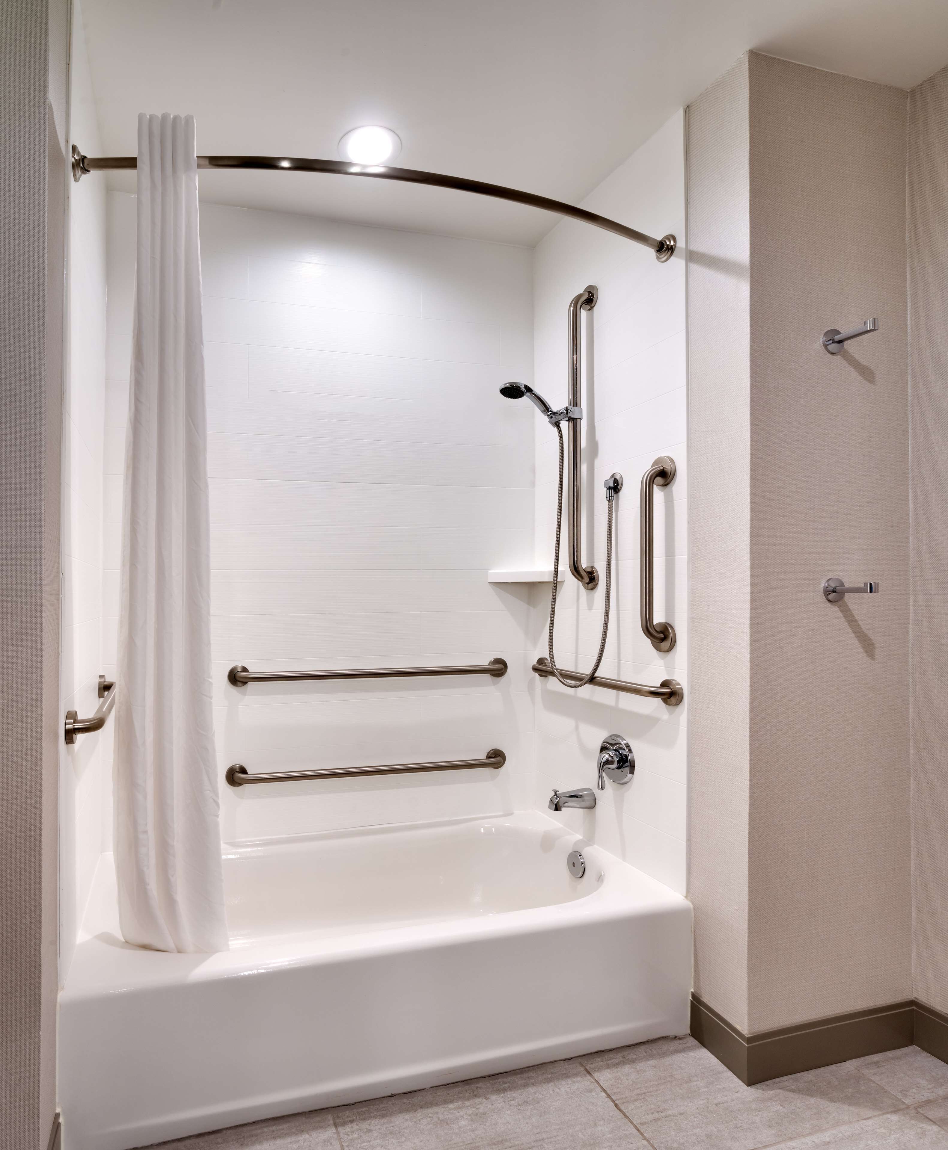 A modern bathroom with a white bathtub, grab bars, a showerhead, and a curtain.