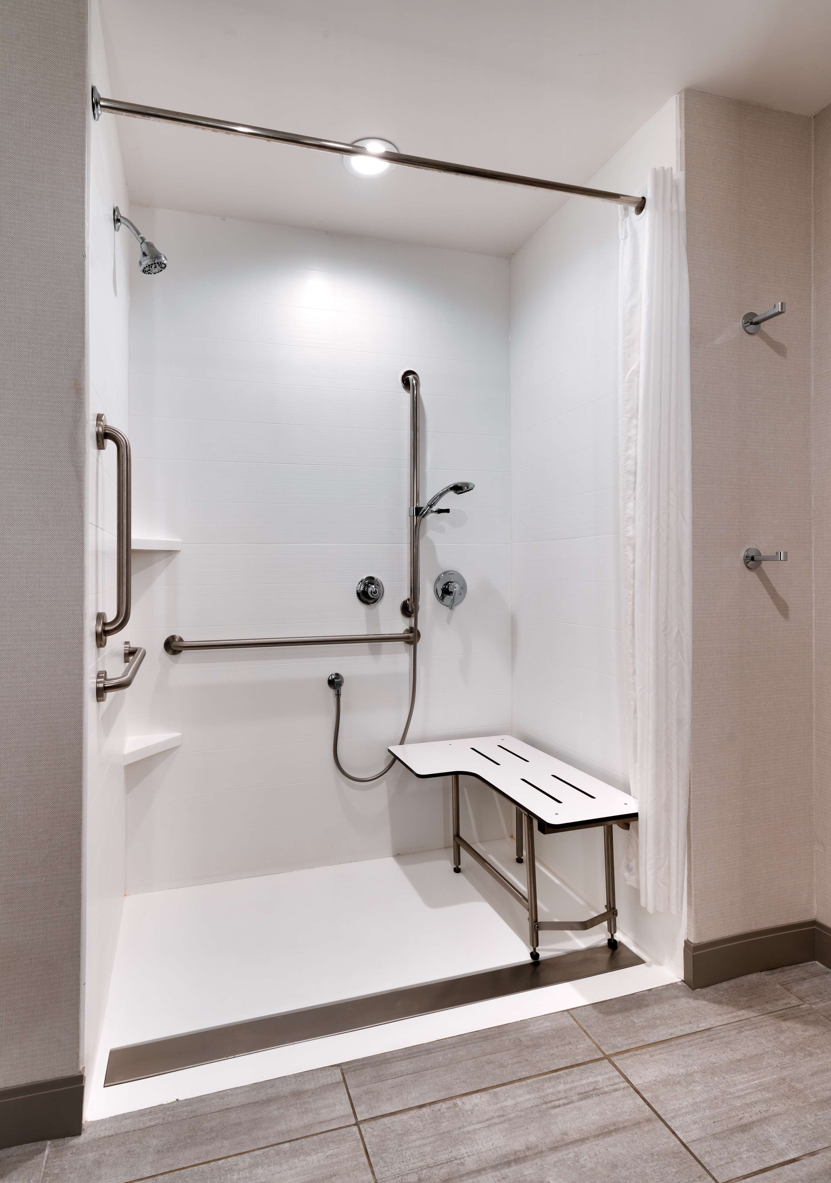A modern shower area with a bench, grab bars, and a handheld showerhead.
