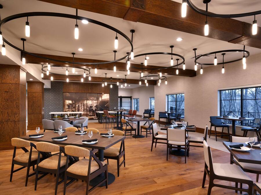 A spacious restaurant with multiple dining areas, wooden floors, and modern pendant lighting.