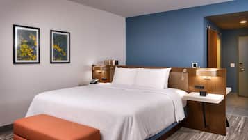 A hotel room with a large bed, a bedside table, a phone, two wall-mounted lamps, and a small orange bench.