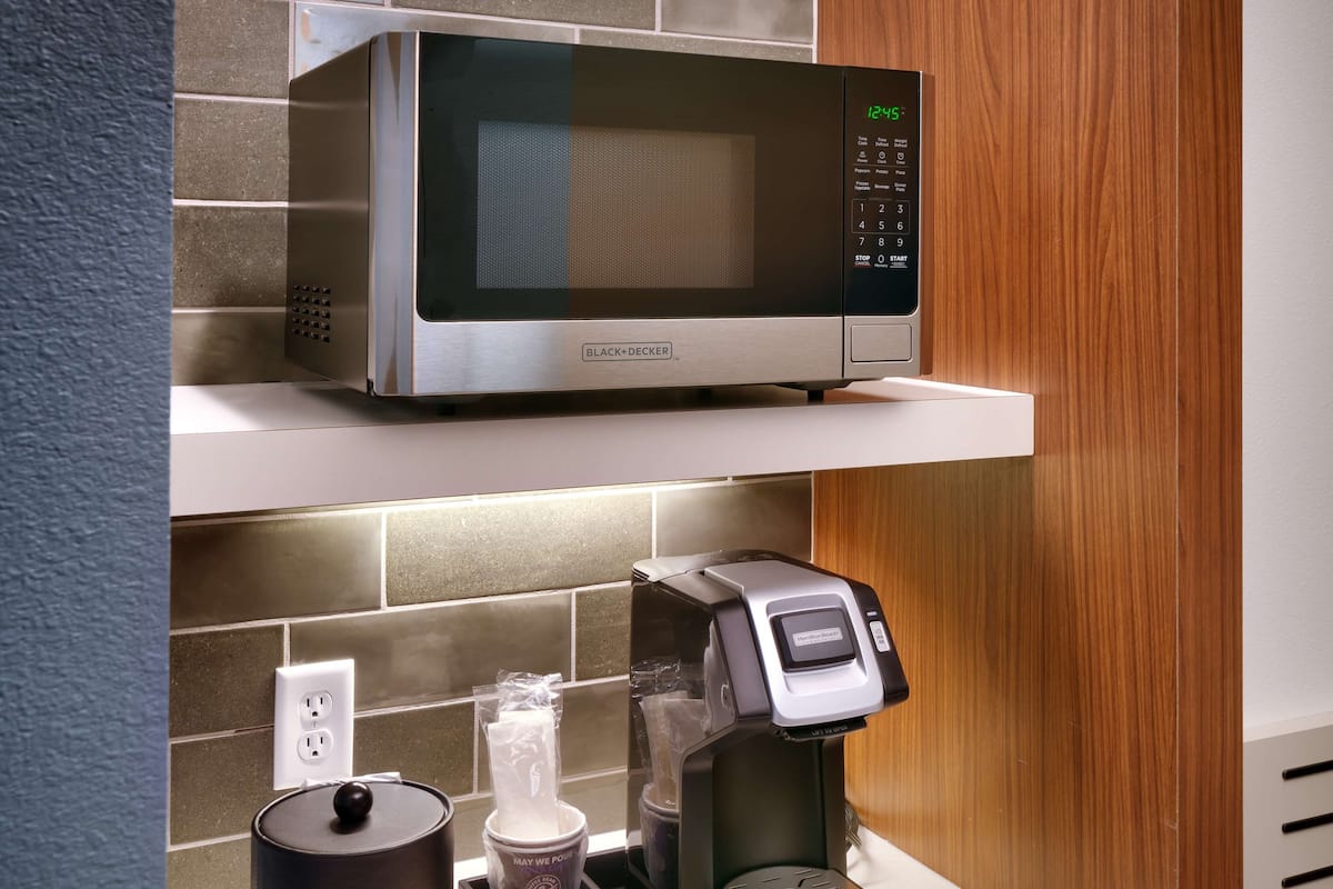 A kitchen area with a microwave on a shelf, a coffee machine, and a container with disposable cups.