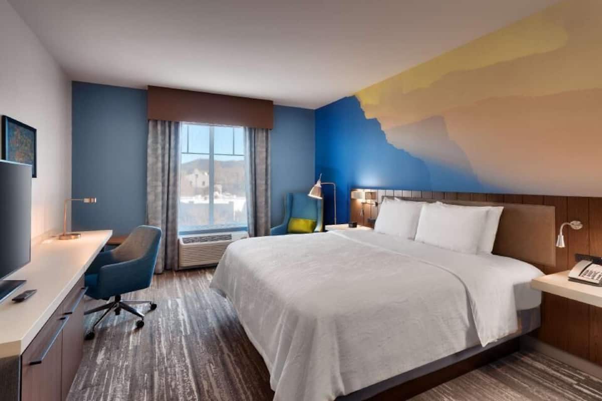 A hotel room with a bed, desk, chair, and a large window.
