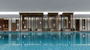 Une piscine intérieure moderne, dotée d’une eau cristalline, de piliers en bois et d’espaces aménagés pour se détendre.