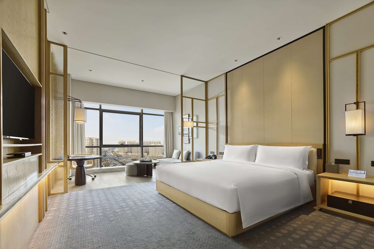 Une chambre d’hôtel moderne dotée d’un grand lit, d’une télévision, d’un bureau et offrant une vue sur la ville.