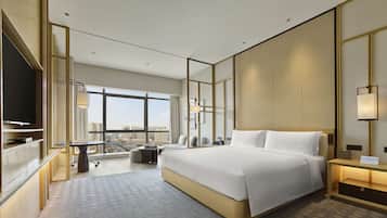 A modern hotel room with a large bed, a TV, a desk, and a view of the city.