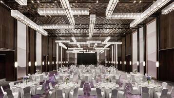 A spacious banquet hall with round tables, white chairs, and a large screen at the front.