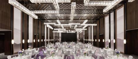 A spacious banquet hall with round tables, white chairs, and a large screen at the front.