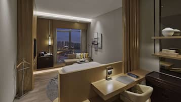 Habitación de hotel moderna con una cama grande, un escritorio, una silla, un baño y vistas de la ciudad al atardecer.