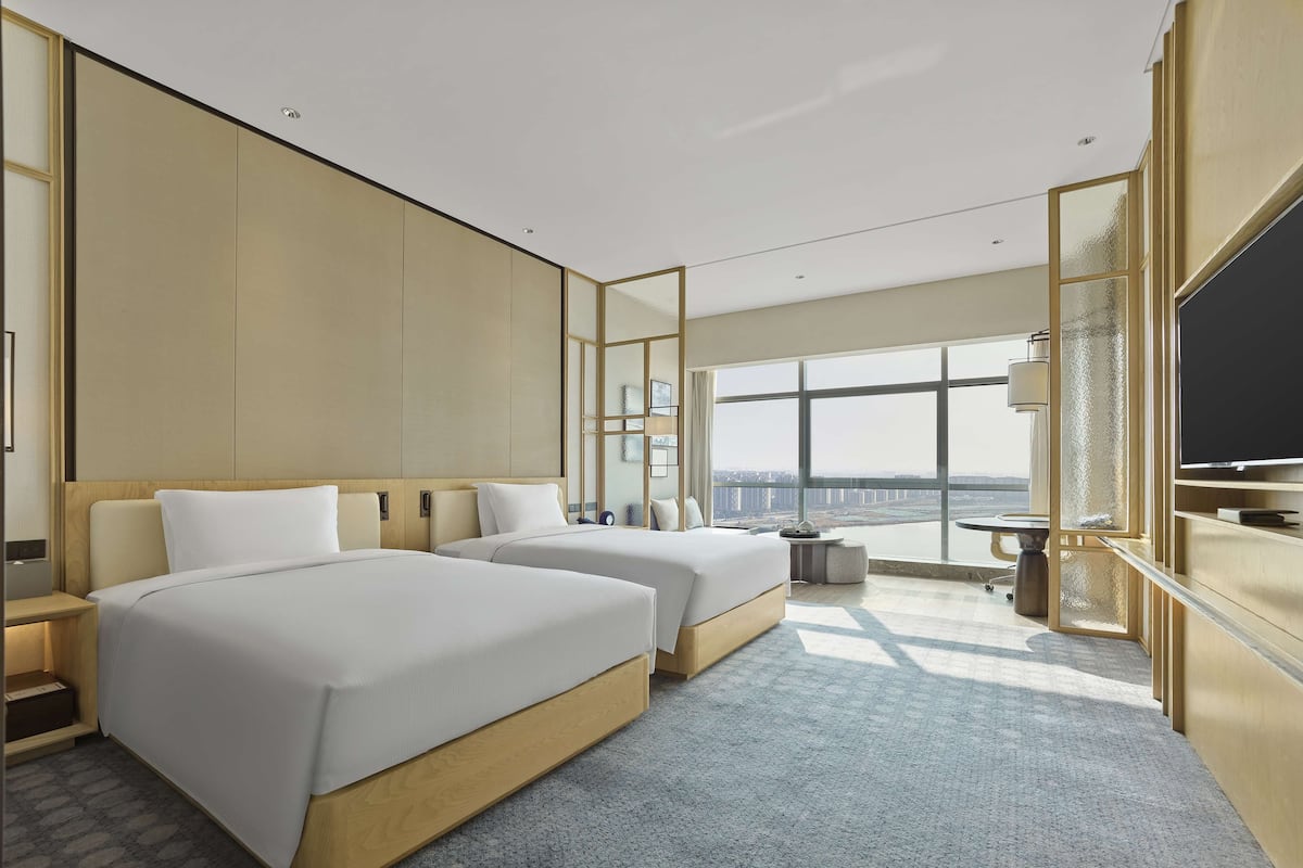 Une chambre d’hôtel moderne avec deux lits, une grande fenêtre donnant sur la ville, un téléviseur à écran plat et une petite table.