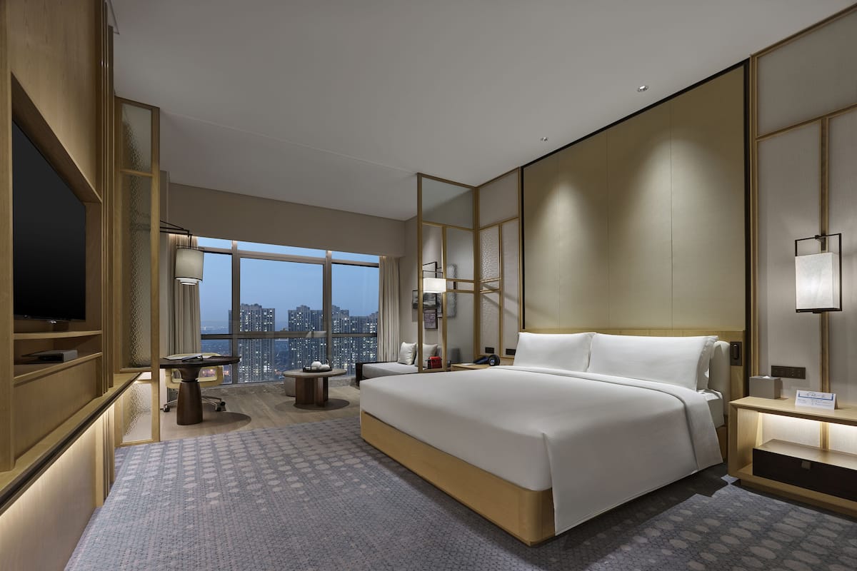 Une chambre d’hôtel moderne dotée d’un grand lit, d’un bureau, d’une chaise, d’une télévision et offrant une vue sur la ville.