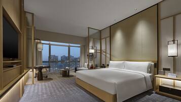 A modern hotel room with a large bed, a desk, a chair, a TV, and a city view.