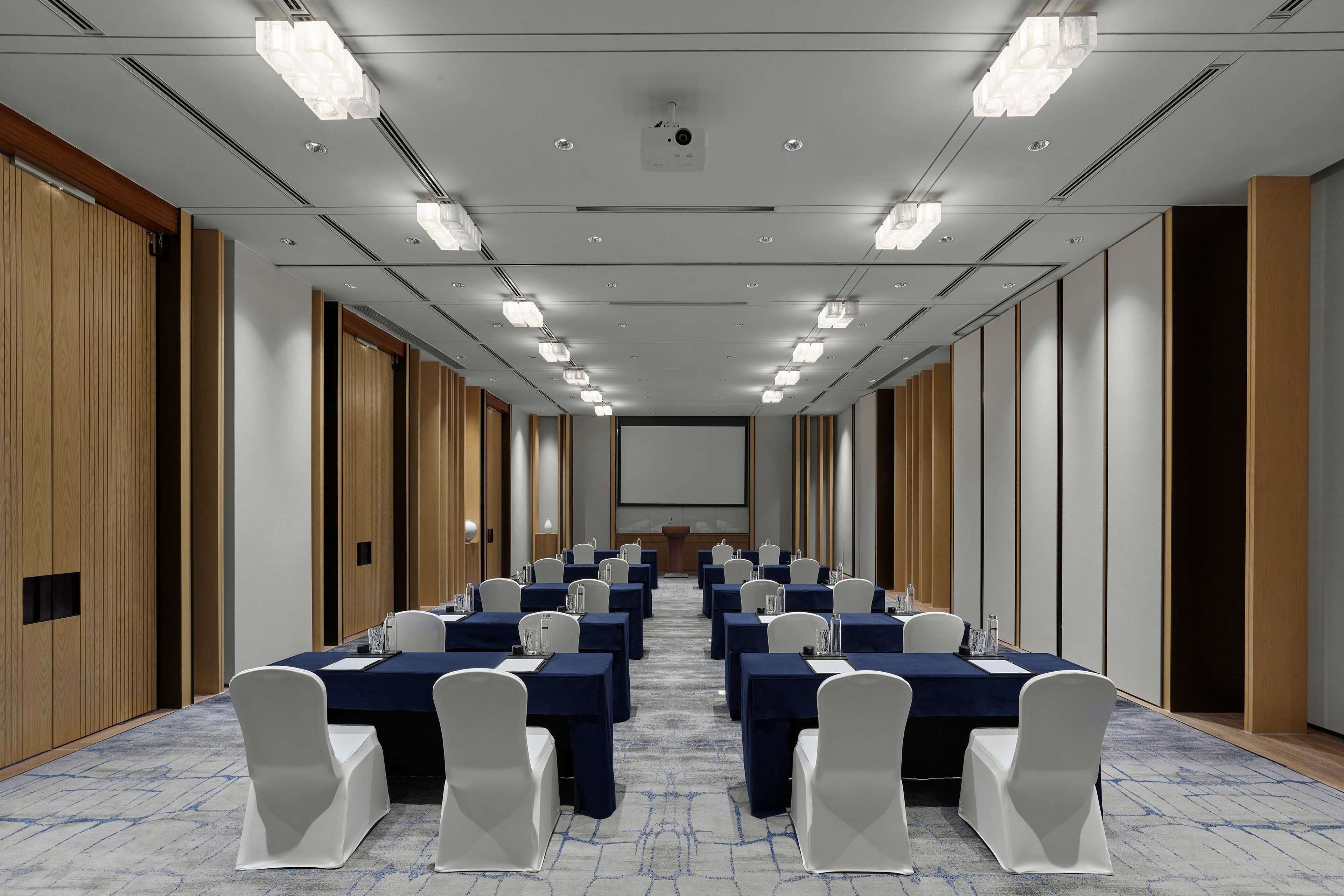 A conference room with rows of tables and chairs, a projector screen, and a podium.