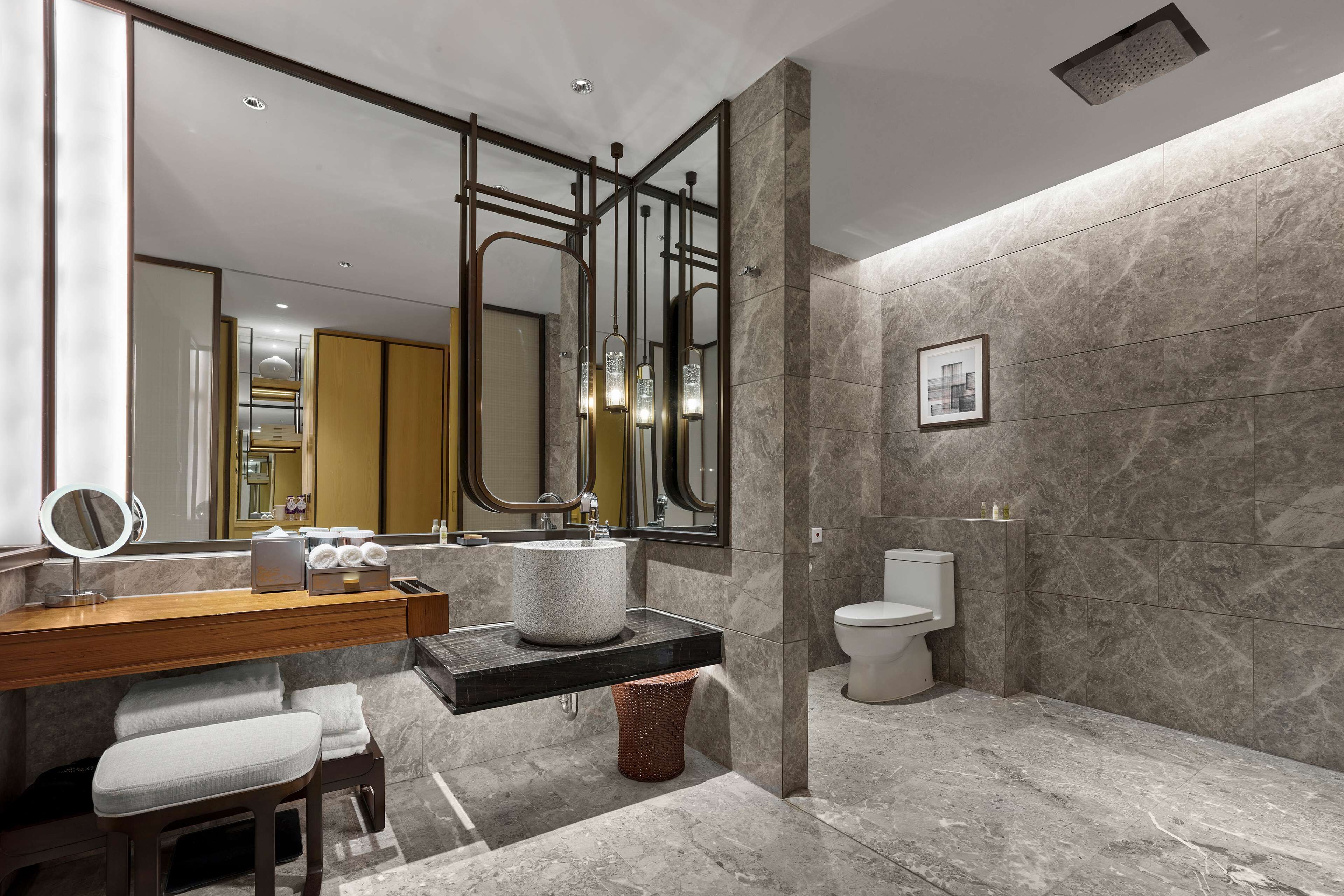 A modern bathroom with a marble floor, a wooden vanity, a round mirror, a sink, and a toilet.
