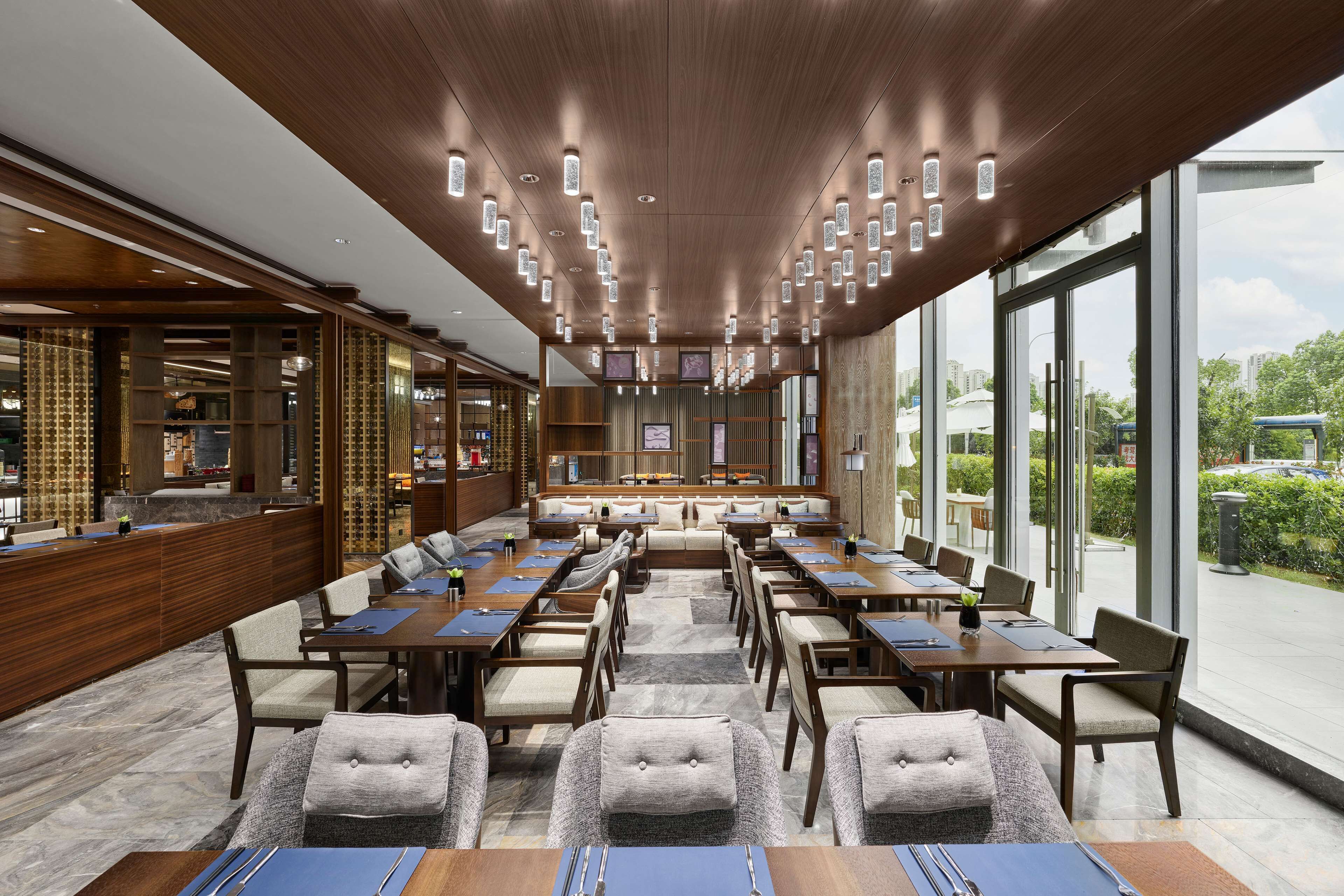 A spacious hotel lobby with a long reception desk, multiple seating areas, and large windows offering a view of the outdoors.
