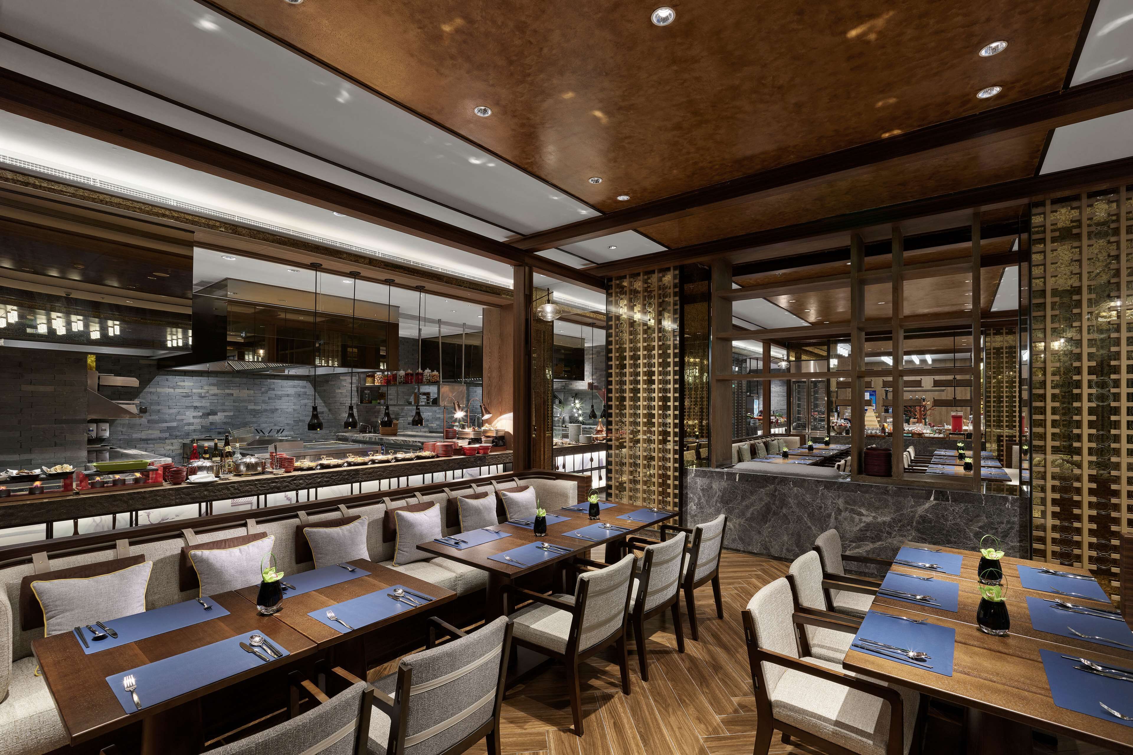 A modern restaurant with long communal tables, individual booths, and a view of the kitchen.