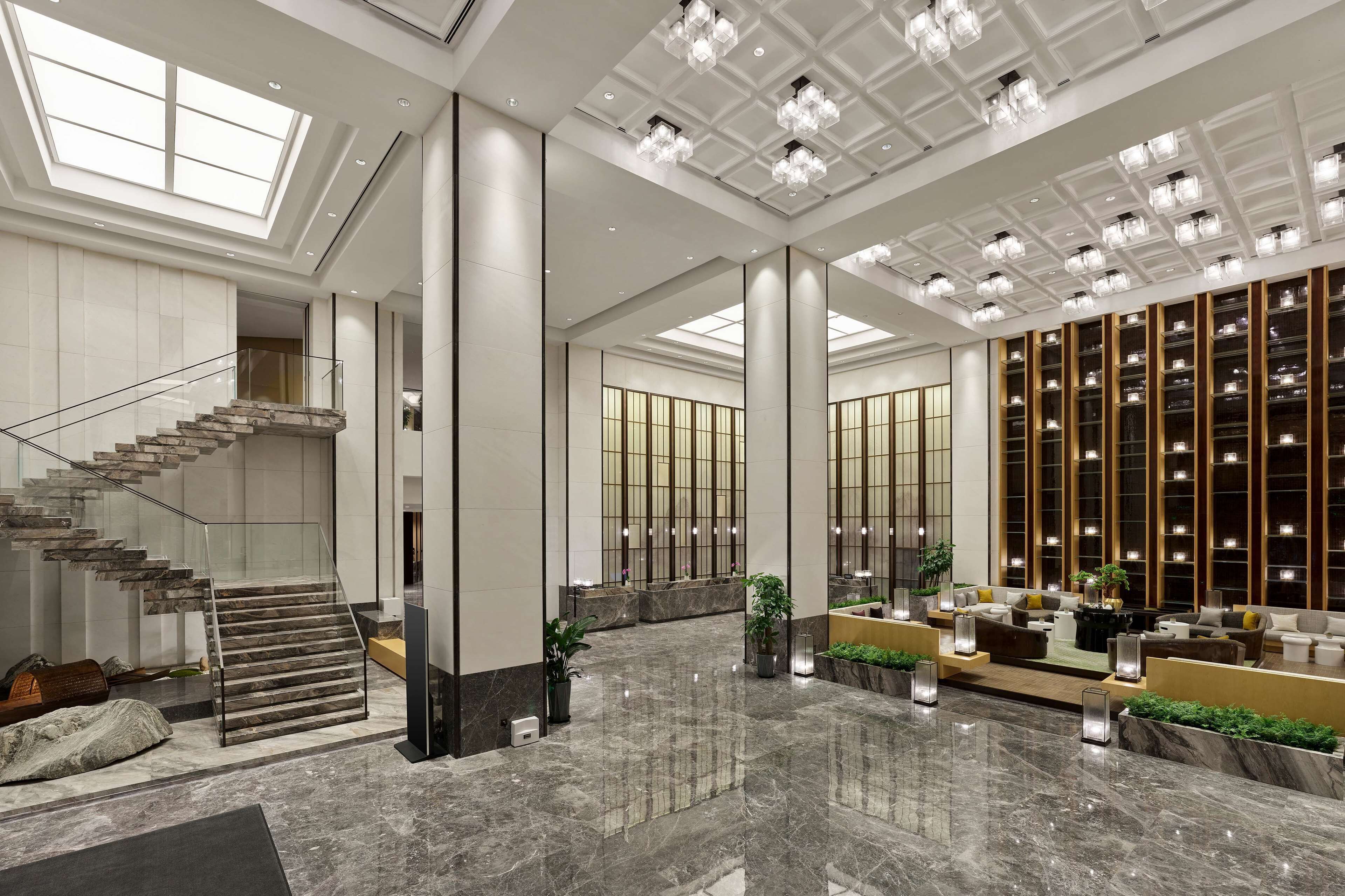 Eine großzügige Lobby mit Marmorboden, einer Treppe und einer Sitzecke mit Sofas und einem Couchtisch.