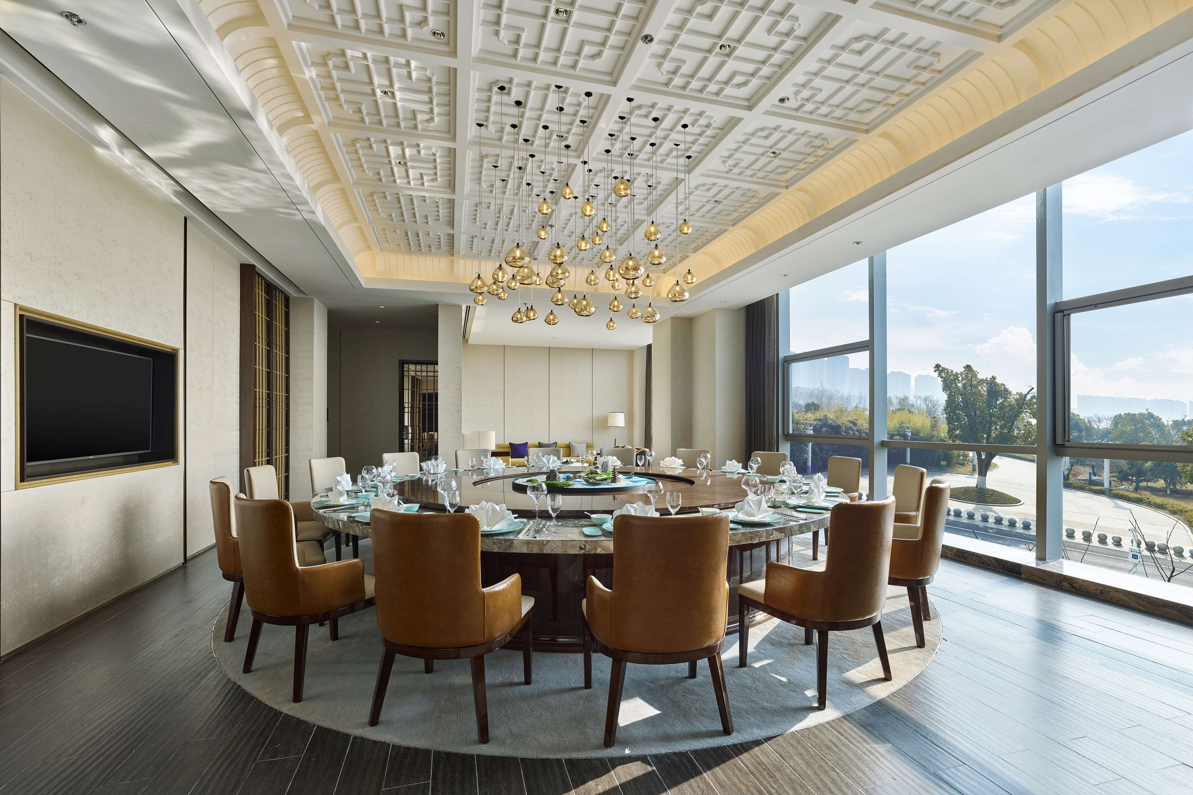 Una sala conferenze moderna con un tavolo rotondo, sedie marroni e un grande lampadario.