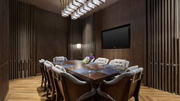Een vergaderruimte met een houten tafel, stoelen, een televisiescherm en een decoratieve lamp.