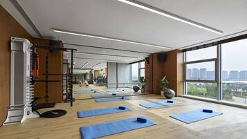 A gym with exercise mats, a squat rack, and a large window with a city view.