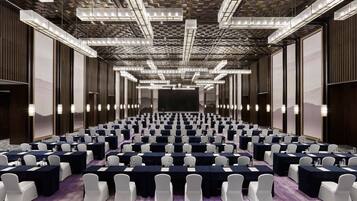 A conference room with rows of tables and chairs, a patterned ceiling, and large windows.