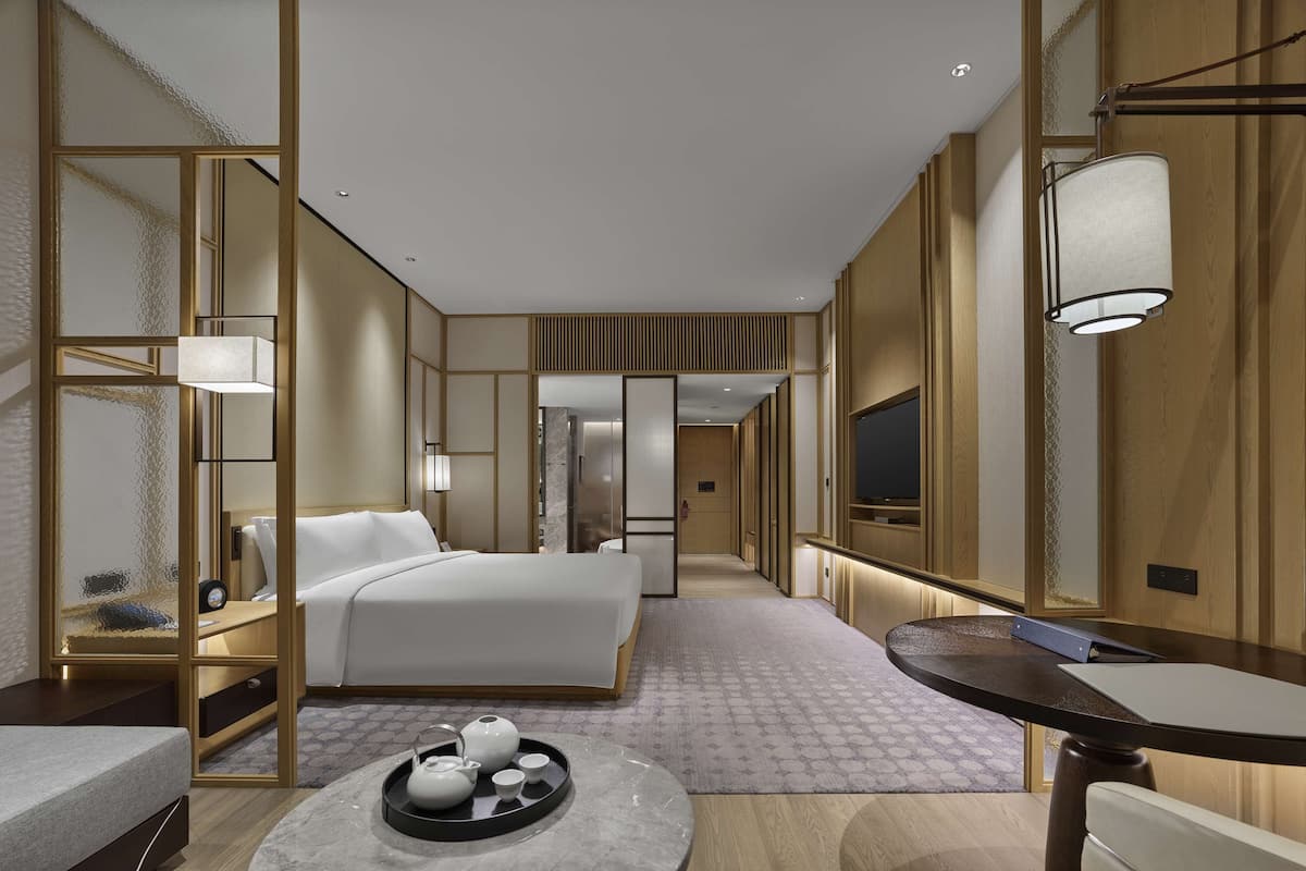 Une chambre d’hôtel moderne avec un grand lit, une table de chevet sur laquelle se trouve un plateau avec du thé, une petite table ronde et un téléviseur fixé au mur.