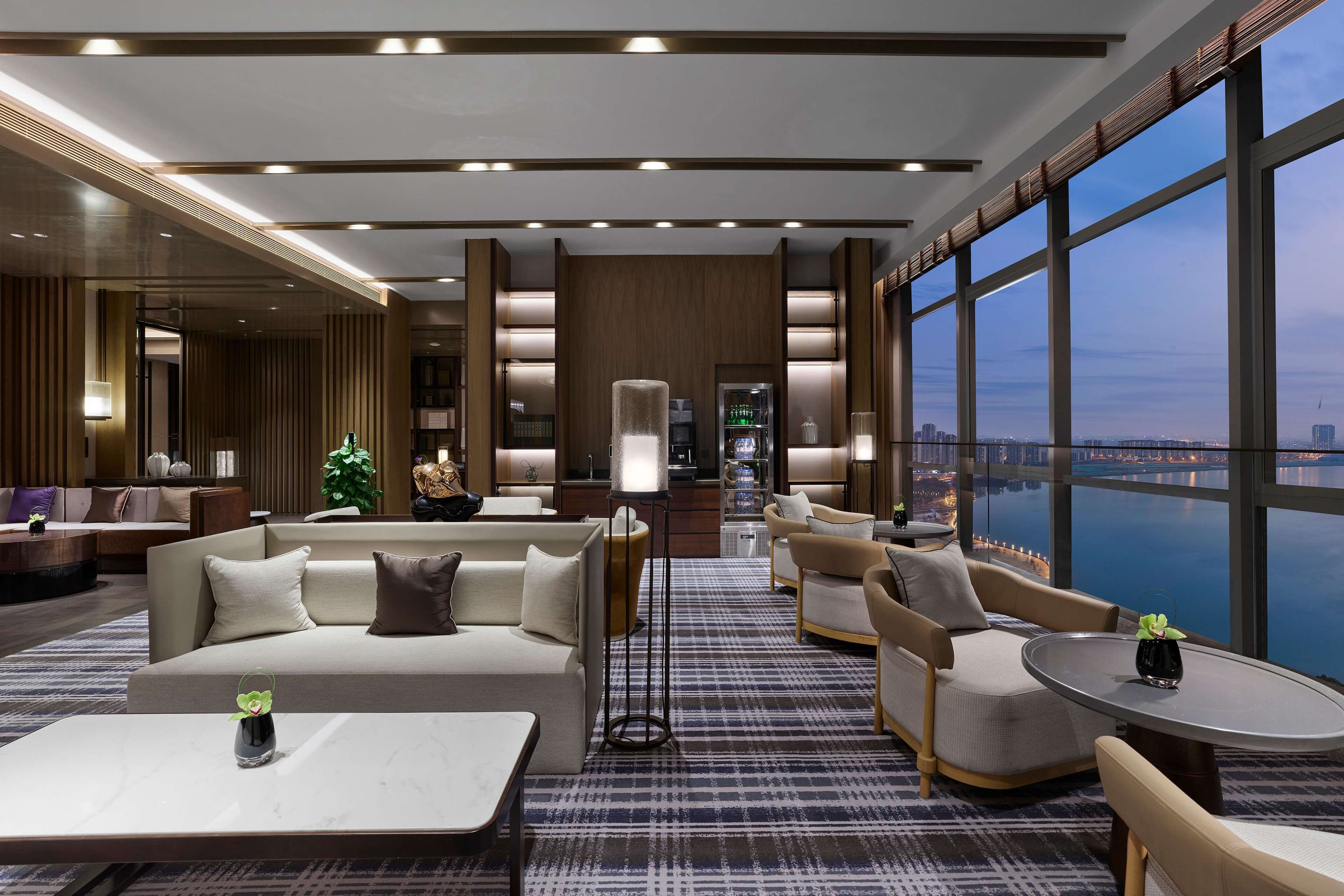 A modern hotel lobby with a sofa, armchairs, a coffee table, and a large window offering a city view.