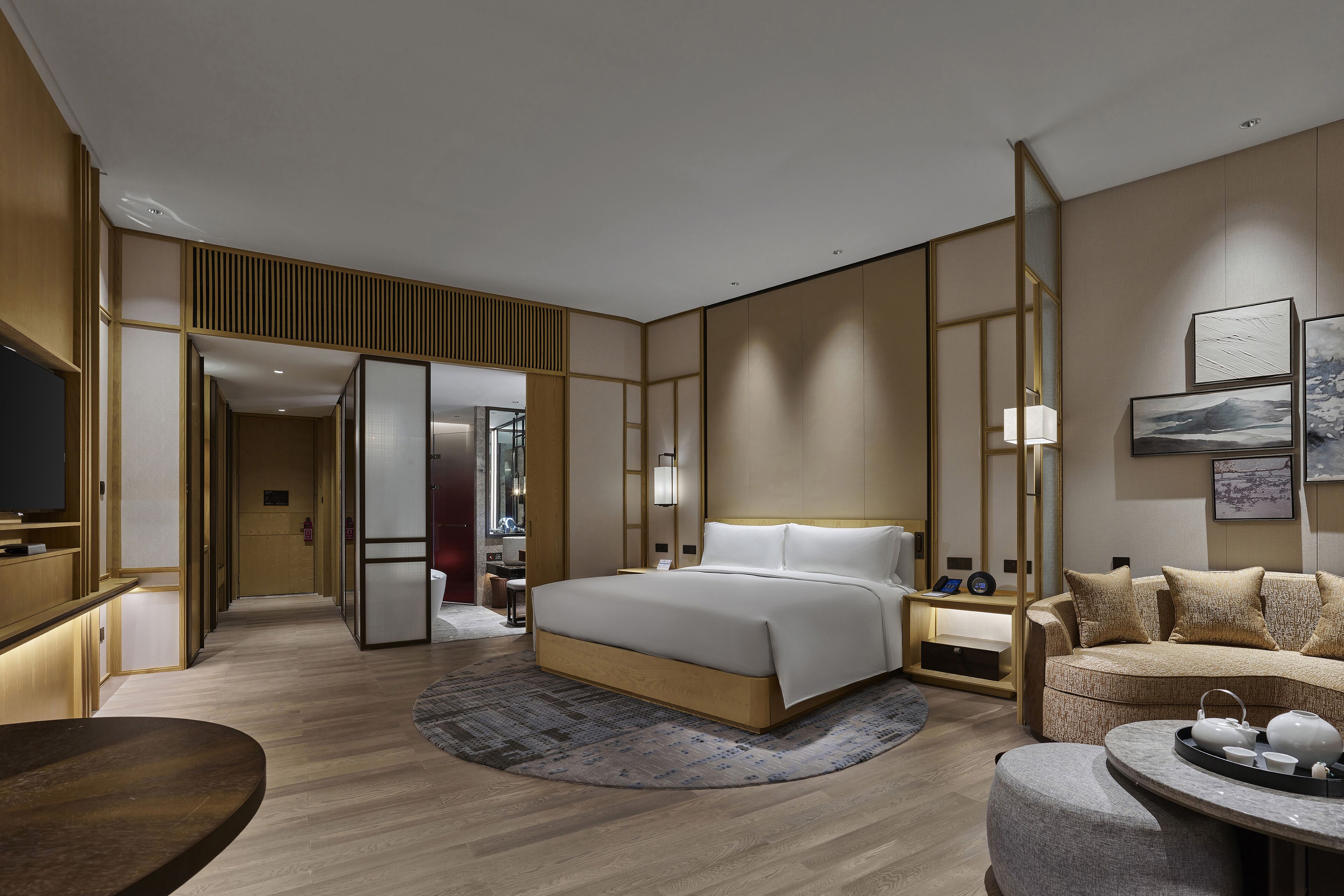 A modern hotel room with a large bed, a sofa, a desk, and a TV.
