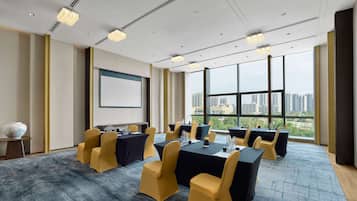 A conference room with a large table, chairs, a projector screen, and a city view through large windows.